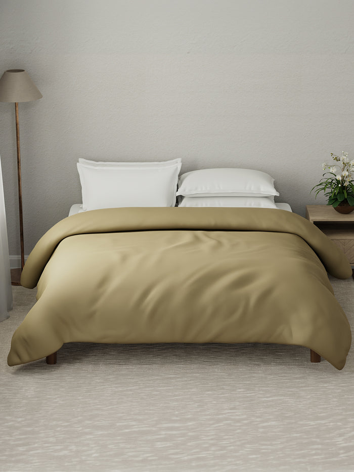 Beige comforter on a bed in a bedroom setting with a lamp and plant.