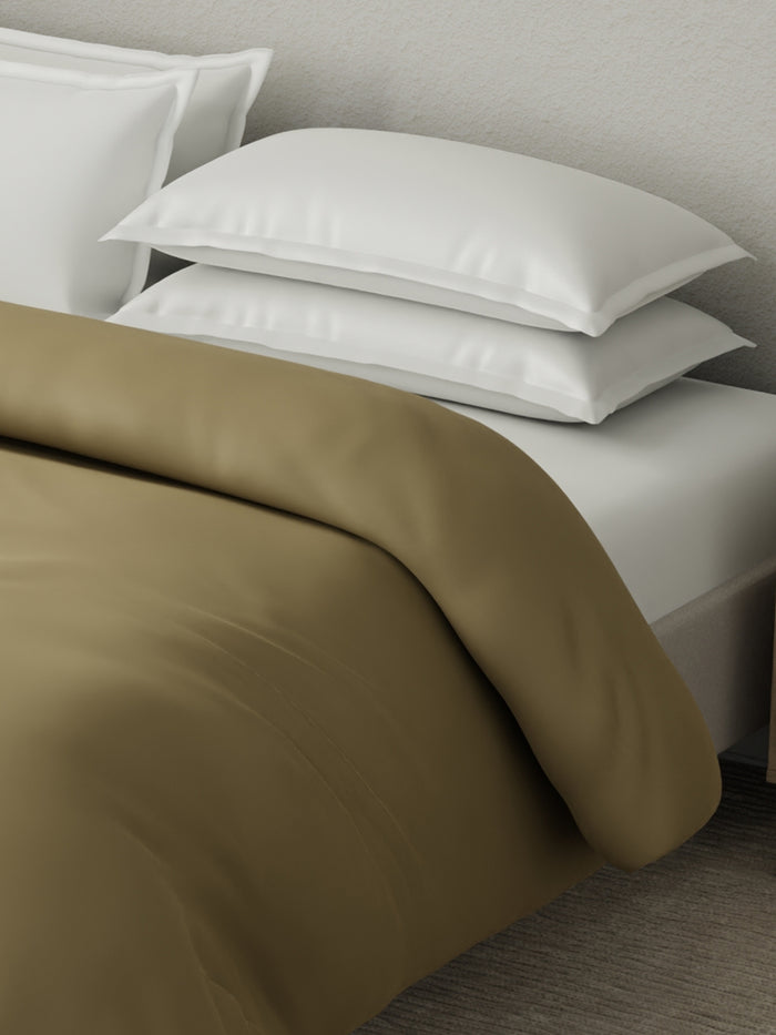 White pillows on a bed with brown bedding against a neutral wall.