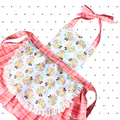 A child's apron with a floral pattern and red checkered trim, featuring a bow tie at the neck.