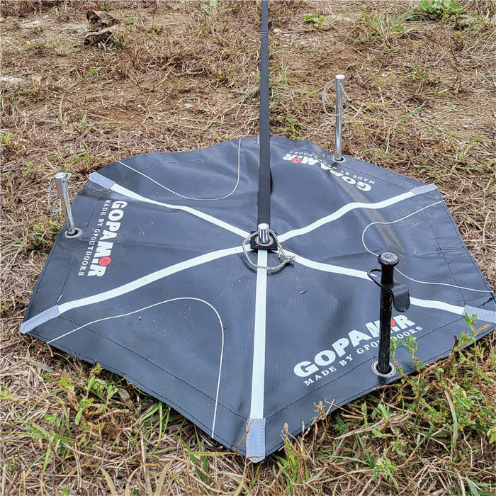 G450 guy-line webbing rising from the center hub of a staked hexagonal Gopamir anchor pad on grassy ground