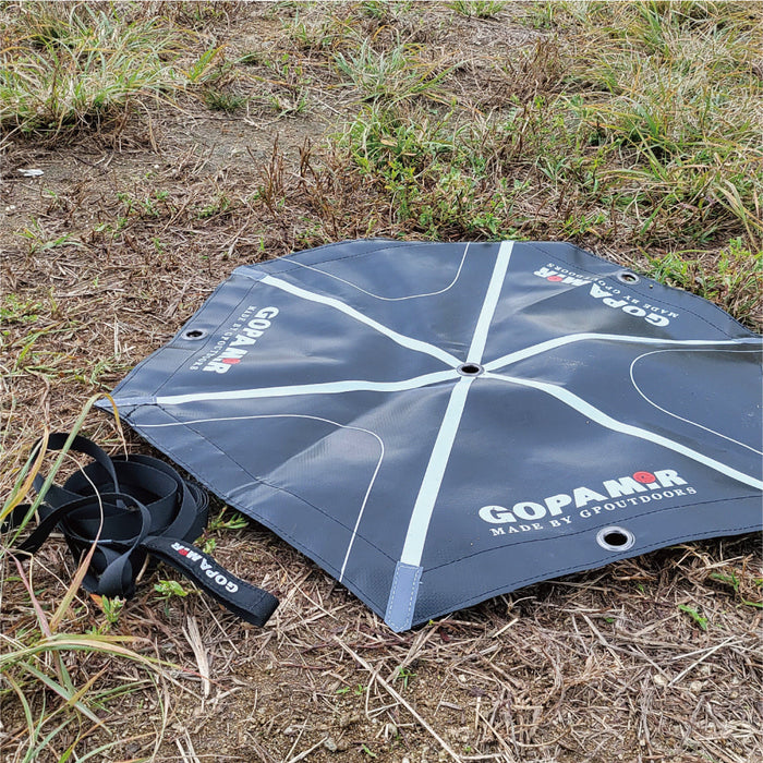 Coiled Gopamir G450 guy-line webbing strap beside the unfolded hexagonal anchor pad on a grassy campsite