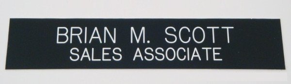 A black rectangular name tape or patch with white text reading 'BRIAN M. SCOTT SALES ASSOCIATE' on a light gray background.