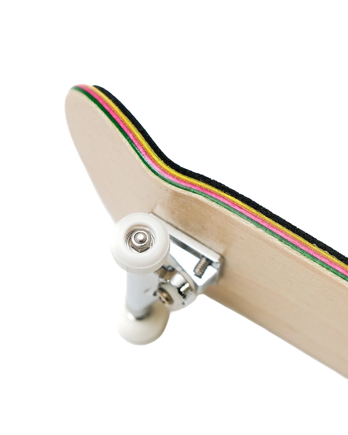 Close-up of a skateboard deck showing the underside, with a light natural wood base, white wheels, and a multicolor striped edge in black, green, yellow, pink, and red on a white background.